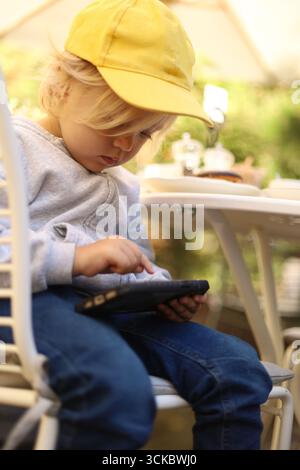 Three-year-old boy in a yellow cap playing a game on a smartphone, children and gadgets Stock Photo