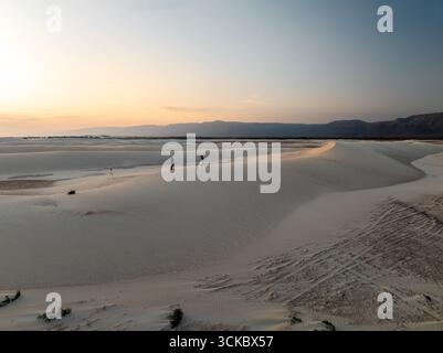 Steroh dunes, Yemen - 23 November 2024: Aerial view of the tranquil, pale sands of Steroh Dunes under a soft, pastel sky, where distant mountains meet the horizon. Stock Photo