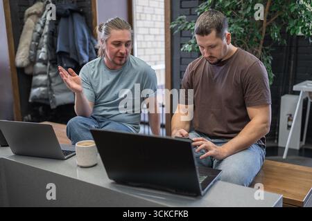 Programmers discussing over laptop working at startup. Office, business and friends together in teamwork with notebook, laptop and coffee workplace Stock Photo