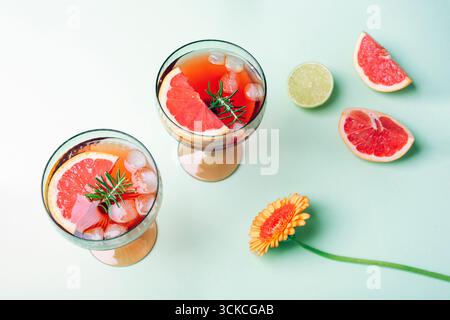 Two glasses of grapefruit cocktail with ice, rosemary and citrus slices on green pastel background. Top view. Stock Photo
