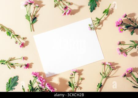 Blank card and small purple flowers on beige background. Top view, flat lay, mockup. Stock Photo