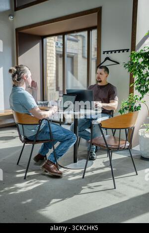 Programmers discussing over laptop working at startup. Office, business and friends together in teamwork with notebook, laptop and coffee workplace Stock Photo