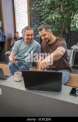 Startup, meeting and team happy in funny, comic and joke time at work with diversity. Office, business and friends together in teamwork with notebook Stock Photo