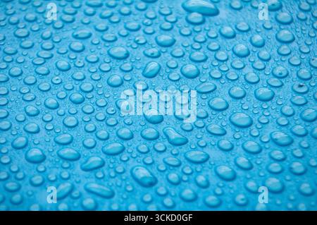 Deep bluish-purple textured surface with evenly distributed water droplets in close up view. Stock Photo