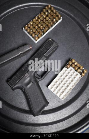 Black semi automatic handgun lying on dark surface next to two open boxes of ammunition and one loaded magazine, showing firearm and bullets arranged for shooting preparation Stock Photo