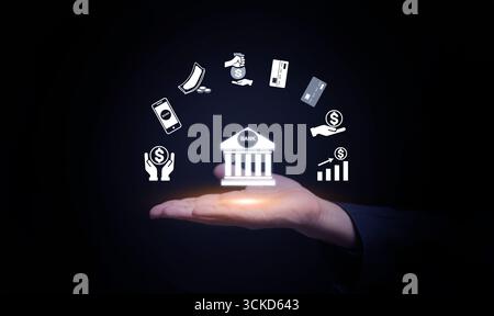 Digital banking concept showing virtual bank icon in human hand, surrounded by money, savings, mobile banking, investment, credit card, and fintech in Stock Photo