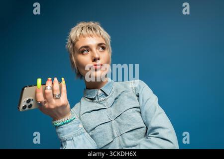 Young woman poses confidently with phone in hand, embracing a cheerful and stylish vibe. Stock Photo