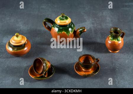 A collection of small tea set pieces, including a teapot, cups, and saucers, are arranged on a grey surface. The tea set is made of clay and has a rus Stock Photo
