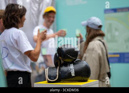 Munich, Germany. 11th Sep, 2025. Boxing gloves lie on a table, people clink plastic cups in the background. Action artists have opened a "pop-up store" in front of the Alte Akademie to sell the possessions of failed Austrian real estate investor and ex-billionaire Benko, which the artists claim to have acquired at an auction of items from his house on Lake Garda. Credit: Leonie Asendorpf/dpa/Ģ����ý Live News Stock Photo