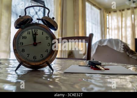Vintage twin bell clock and car keys on a table in a room with sunlight filtering through blinds and windows Stock Photo