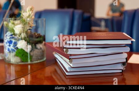 Stack of books on conference table with glass vase and floral arrangement. Stock Photo