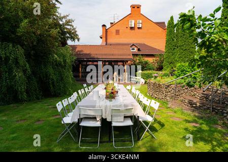 Outdoor garden wedding setup with elegant table arrangement and rustic brick building. Stock Photo