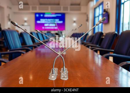 Empty conference room with microphones on long wooden table in bright office setting. Stock Photo