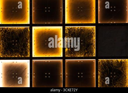 Wall made of decorative tiles with internal illumination in yellow and white with dark areas. Stock Photo