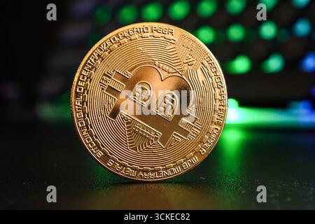 Golden cryptocurrency coin displayed on a dark surface with colorful lights in the background Stock Photo