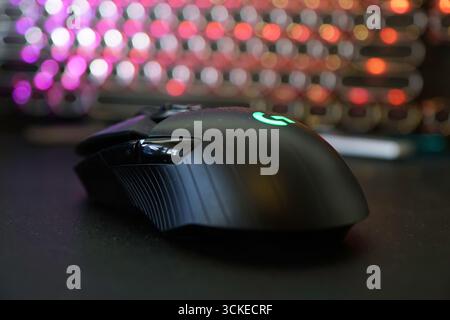 Sleek black gaming mouse illuminated with green LED sits on a dark surface in a vibrant gaming setup Stock Photo