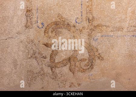 Warm‑tinted plaster surface showing subtle brush, trowel marks and a faded ornamental fresco motif for authentic vintage character. Useful as rustic b Stock Photo