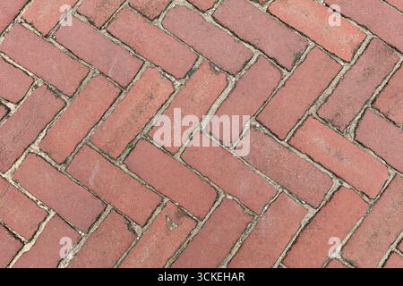 Red clay brick pavers arranged in a classic herringbone pattern with visible mortar and natural wear. Crisp overhead texture ideal for backgrounds, CA Stock Photo