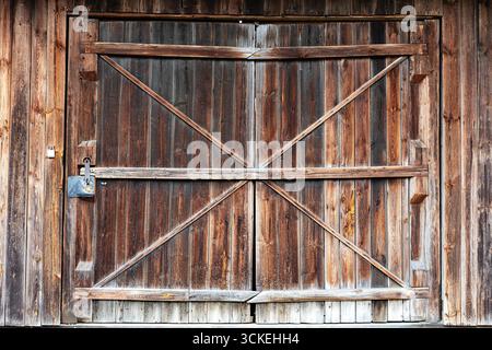 Pair of rustic sliding barn doors with X‑braced timbers and a simple metal latch set in a weathered plank facade. Rural construction detail ideal for Stock Photo