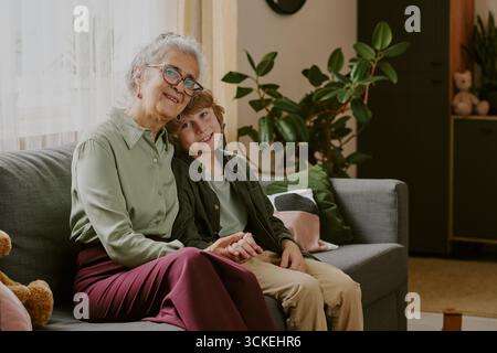Senior Caucasian Woman Sitting with Smiling Caucasian Boy on Sofa Indoors Stock Photo