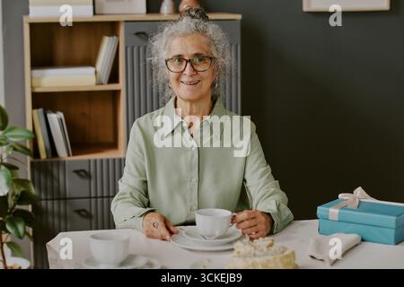 Portrait of Senior Caucasian Woman Smiling While Sitting at Table Drinking Tea Stock Photo