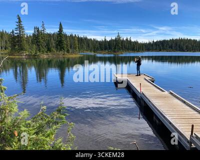 Woman taking photos from a wooden dock at Battleship Lake in Strathcona Provincial Park, Vancouver Island, British Columbia, Canada under a clear sky. Stock Photo