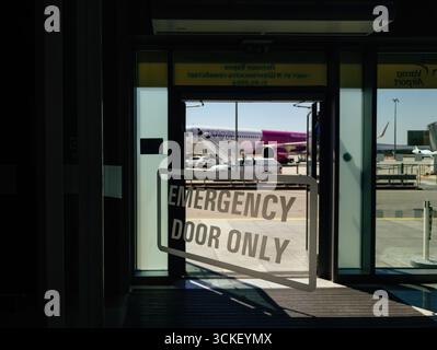 Varna, Bulgaria - Aug 24, 2025: View from inside Varna Airport showing an emergency exit door with signage, overlooking the tarmac where a passenger a Stock Photo