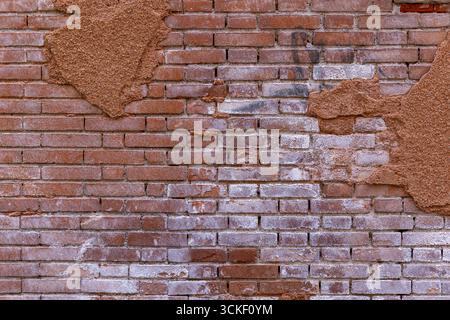 Old weathered brick wall with peeling plaster. Close-up of an aged brick wall with patches of crumbling plaster and visible white staining, showing Stock Photo