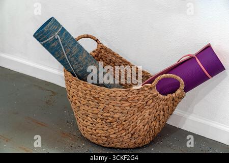 Colorful Yoga mats rolled up in a decorative, braided, woven natural fiber basket on the floor Stock Photo