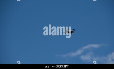 Small drone captured in flight against a clear blue sky with a few clouds. The image can be used for themes of aerial technology, remote piloting, inn Stock Photo