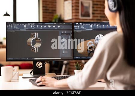 Close up of female engineer with headphones, designing metal prototype using CAD software on dual monitors in home studio. Remote, technical and modern workspace setup for professional woman developer Stock Photo