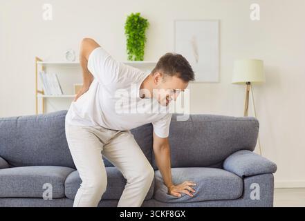 Man suffering sharp lower back pain while standing up from couch at home Stock Photo