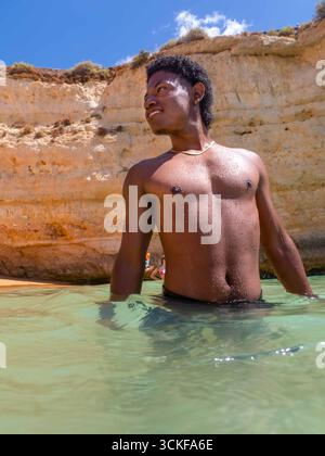Young African American man swims in ocean in Algarve Portugal Sea da Rocha Beach Stock Photo