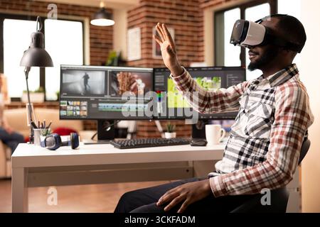Black filmmaker editing multimedia video with vr glasses and advanced software. African american male editor working from home, using virtual reality tools in completing post production movie project. Stock Photo