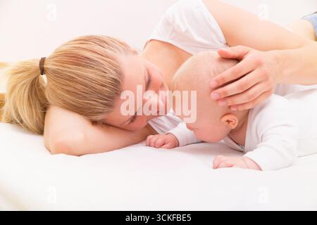 Baby lying on its tummy and lifting its head, mum lying next to it and stroking its head Stock Photo