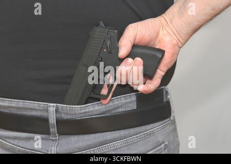 A man holstering a gun in the waisteband Stock Photo