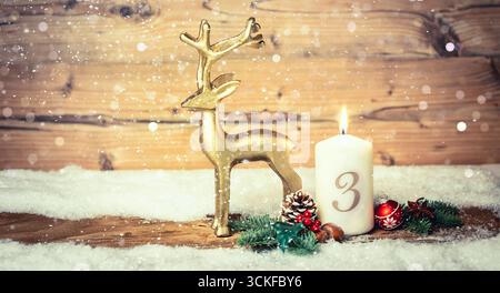 Christmas decoration with a burning candle and golden reindeer figure, 3rd Advent Stock Photo