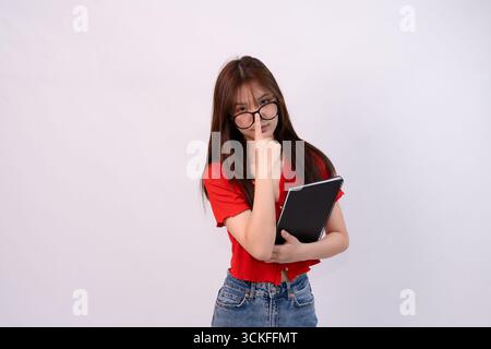 young woman wearing glasses holding notebook against plain background Stock Photo