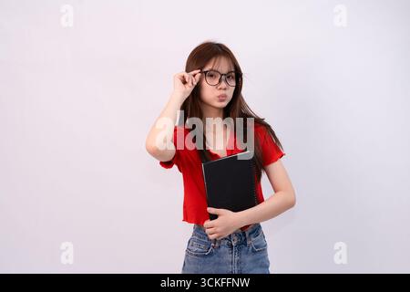 young woman wearing glasses holding notebook against plain background Stock Photo