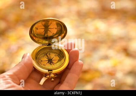 Closeup of a woman’s hand holding an old-fashioned golden compass outdoors with defocused autumn background. Symbol of navigation, exploration, direct Stock Photo