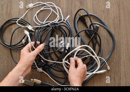 Closeup of woman’s hands organizing a pile of assorted cables and cords. Concept of technology clutter, electronic organization, recycling, and modern Stock Photo