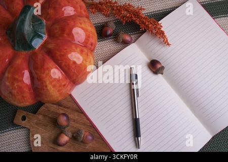 Autumn planning flat lay: open lined notebook and pen, ceramic pumpkin, acorns and dried flowers on knitted fabric and wooden board — cozy seasonal Stock Photo