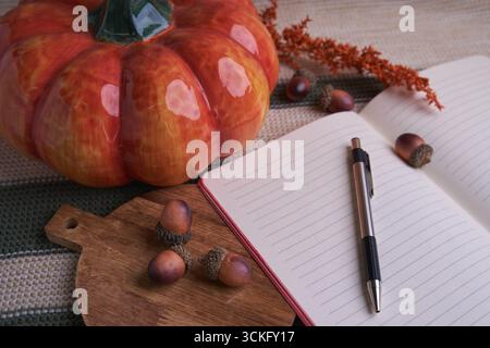 Autumn planning flat lay: open lined notebook and pen, ceramic pumpkin, acorns and dried flowers on knitted fabric and wooden board — cozy seasonal Stock Photo