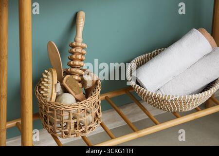 Wicker baskets with different massage body brushes and clean towels on shelf in room, closeup Stock Photo