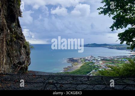A dramatic clifftop near Sanbanggulsa Temple overlooks the Jeju shoreline, showing storm light over the rocky coast and fishing villages. Stock Photo