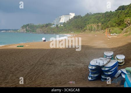 Stacks of soft‑top surfboards rest on the upper beach after lessons while dark clouds gather offshore and a resort and lifeguard tower overlook the ba Stock Photo