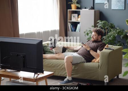 Young Adult Man Relaxing on Sofa with Dog Watching Television Stock Photo