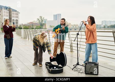 Group of young adults performing live music outdoors, Caucasian man playing guitar, young woman singing into microphone Stock Photo