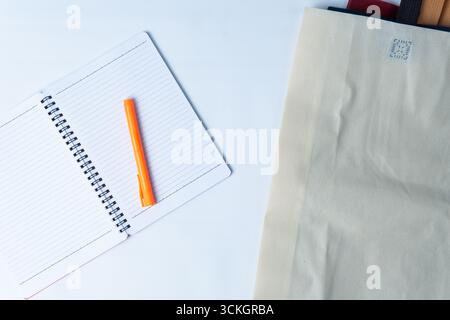 Open spiral notebook with an orange marker placed on lined pages, beside a folded eco bag on a white desk. Stock Photo