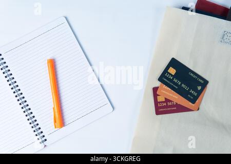 Flat lay of an open notebook with an orange marker beside an eco bag containing three mockup credit cards. Stock Photo